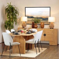 a dining room table with white chairs and a potted plant on the sideboard