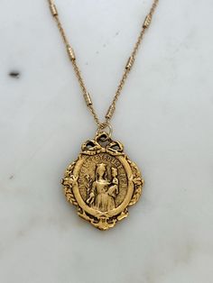 ✨ Our Lapeyrouse French Mary Necklace is a vintage-inspired pendant that captures the elegance of the early 1900s Art Nouveau style. It features a charming bow atop an image of Mary and Child, adorned with a delicate antiqued gold ribbon. On the back, you'll find the Church of Notre Dame of Lapeyrouse, located in the beautiful Occitanie region of Southern France.  ✨ Experience the grace of our Virgin Mary Pendant Necklace. Order now and add a touch of divine beauty to your collection.  Size and Mother Mary Jewelry, Antique Necklaces With Vintage Charm And Round Pendant, Vintage Medallion Necklace With Coin Pendant For Gift, Antique Medallion Necklace For Vintage Events, Antique Gold Medallion Necklace, Heirloom Necklace With Antique Finish For Vintage Collection, Vintage Antique Gold Medallion Necklace As Gift, Vintage Coin Pendant Necklace For Wedding, Antique Gold Vintage Medallion Necklace As Gift