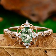 an oval shaped green and white diamond ring sitting on top of a leaf covered surface