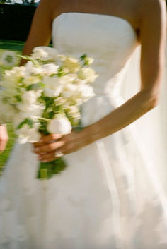 a woman in a wedding dress holding a bouquet of white flowers on her left hand