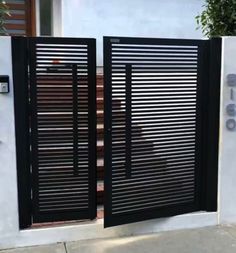 an open gate with black slats on the side of a white wall and steps