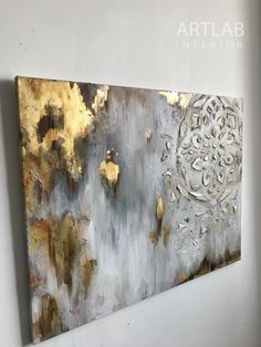 an abstract painting hanging on the wall next to a white wall with gold leaf designs