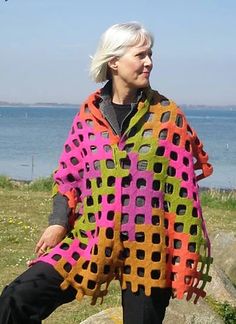 a woman standing on top of a rock next to the ocean wearing a colorful poncho