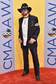 a man in a black hat and suit on the red carpet at an awards event