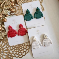 three pairs of red and green earrings sitting on top of a table next to a gold ornament