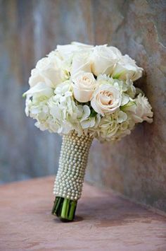 a bridal bouquet with white flowers and pearls on the end is placed against a stone wall