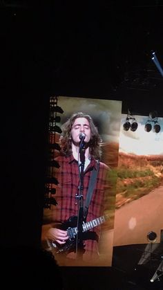 a man on stage with a guitar and microphone in front of an image of a road