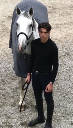 a man standing next to a white horse with a black cover on it's head