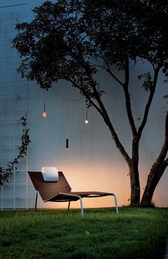 a lawn chair sitting in the grass under a tree with lights hanging from it's branches