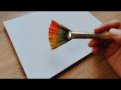 someone is holding a paint brush over a piece of paper with the color red and yellow on it