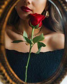 a woman holding a red rose in front of her face and looking at the mirror