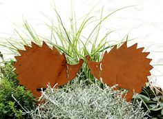 two metal leaves sitting on top of green plants and grass in front of a white wall