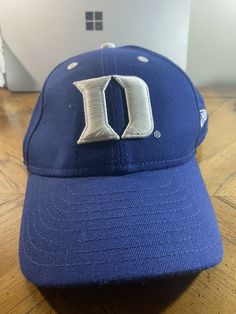 a blue hat with the letter d on it sitting on a wooden floor next to a laptop