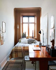 a bed sitting next to a window in a bedroom under a wooden desk with a laptop on it