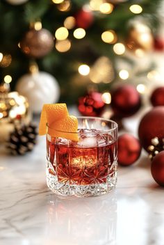 an old fashioned cocktail with orange peel and garnish in front of a christmas tree