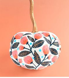 a white pumpkin with orange and blue leaves on it's side, against a pink background