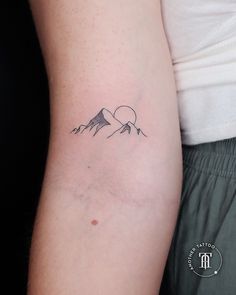 a person with a small tattoo on their arm and the mountain behind them is shown