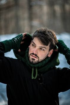 a man with a green scarf on his head standing in front of some snow covered trees