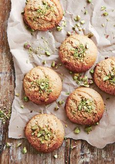 five cookies with pistachio on top sitting on a piece of parchment paper