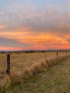 the sun is setting behind a fence in an open field with cows grazing on it