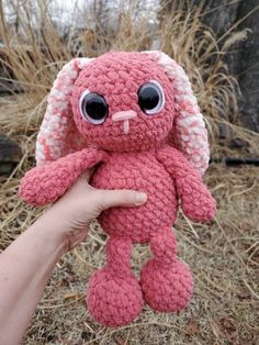 a hand holding a pink crocheted stuffed animal with big eyes and an ear