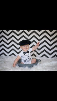 a baby sitting in a bowl wearing a black hat and white shirt with the number 12 on it