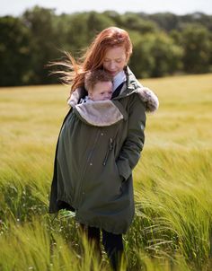 a woman holding a baby in her arms while walking through tall grass with trees in the background