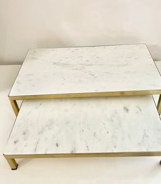 two white marble coffee tables with gold metal legs on each side, against a plain white wall