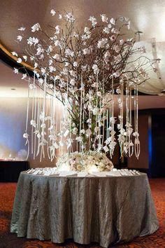 an elegant centerpiece with white flowers and branches is displayed on a round table in the middle of a room