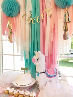 a llama cake and cupcakes on a table with tissue pom poms