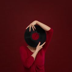 a woman in a red dress holding a black record up to her face with both hands