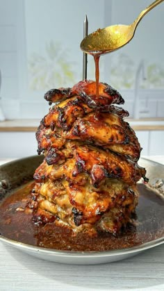 a stack of food on a plate with a spoon and sauce being poured over it