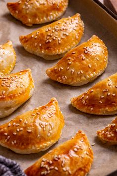 several pastries are lined up on a baking sheet with sesame seed sprinkles