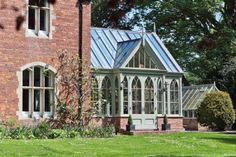 an old brick house with a metal roof and glass windows in the front yard, surrounded by greenery