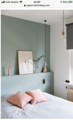 a bed with two pink pillows on top of it next to a wall mounted light