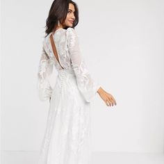 a woman wearing a white dress with sheer sleeves and open back, standing in front of a