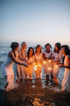 a group of women standing in the ocean holding sparklers and looking at the camera