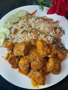 a white plate topped with chicken and rice next to cucumbers on a table