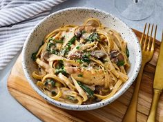 a white bowl filled with pasta, mushrooms and spinach on top of a wooden cutting board