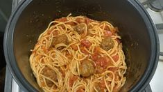 spaghetti with meatballs and tomato sauce in a pot on the stove top, ready to be cooked