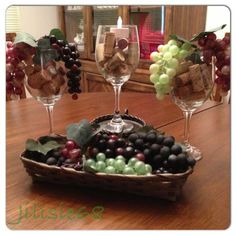 two wine glasses and some grapes in a basket on a table with other items around it