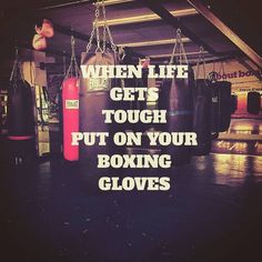 a gym with boxing gloves hanging from the ceiling and a quote written on it that says when life gets tough, put on your boxing gloves