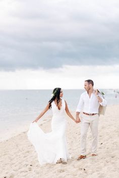 a bride and groom walking on the beach holding hands