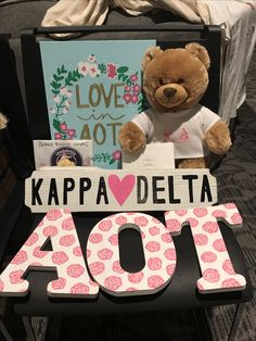 a brown teddy bear sitting on top of a chair next to a sign that says kapa delta