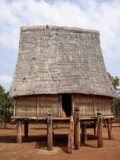 a hut with thatched roof and wooden pillars in front of it on dirt ground