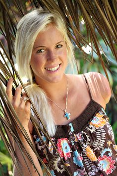 a beautiful blonde woman standing under a palm tree