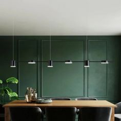 a dining room with green walls and wooden table surrounded by black leather chairs, potted plants and hanging lights