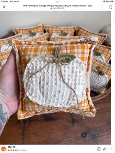 a hand holding a small pumpkin pillow on top of a wooden table next to other pillows