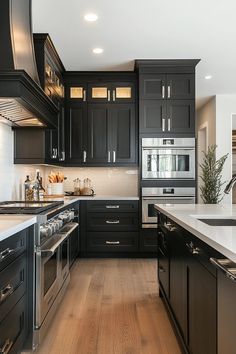 a large kitchen with black cabinets and white counter tops, stainless steel appliances and wood flooring