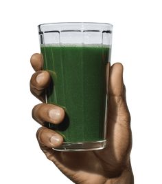 a hand holding a glass filled with green smoothie on top of a white background